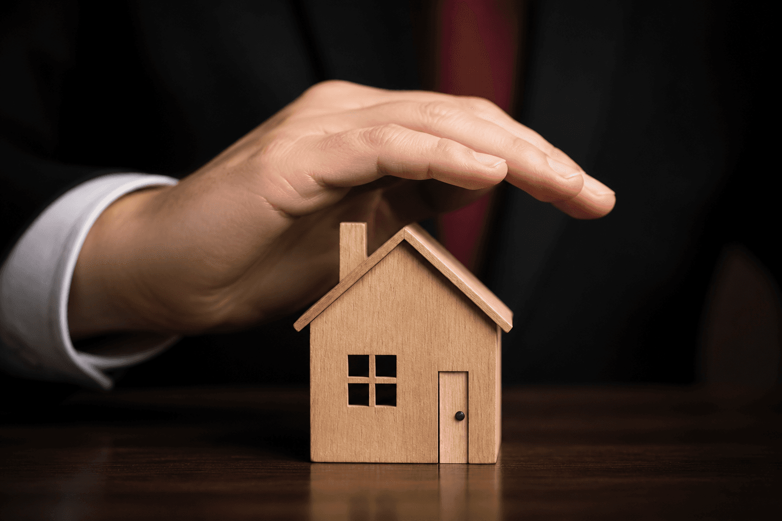 Hand protectively covering a small wooden house model
